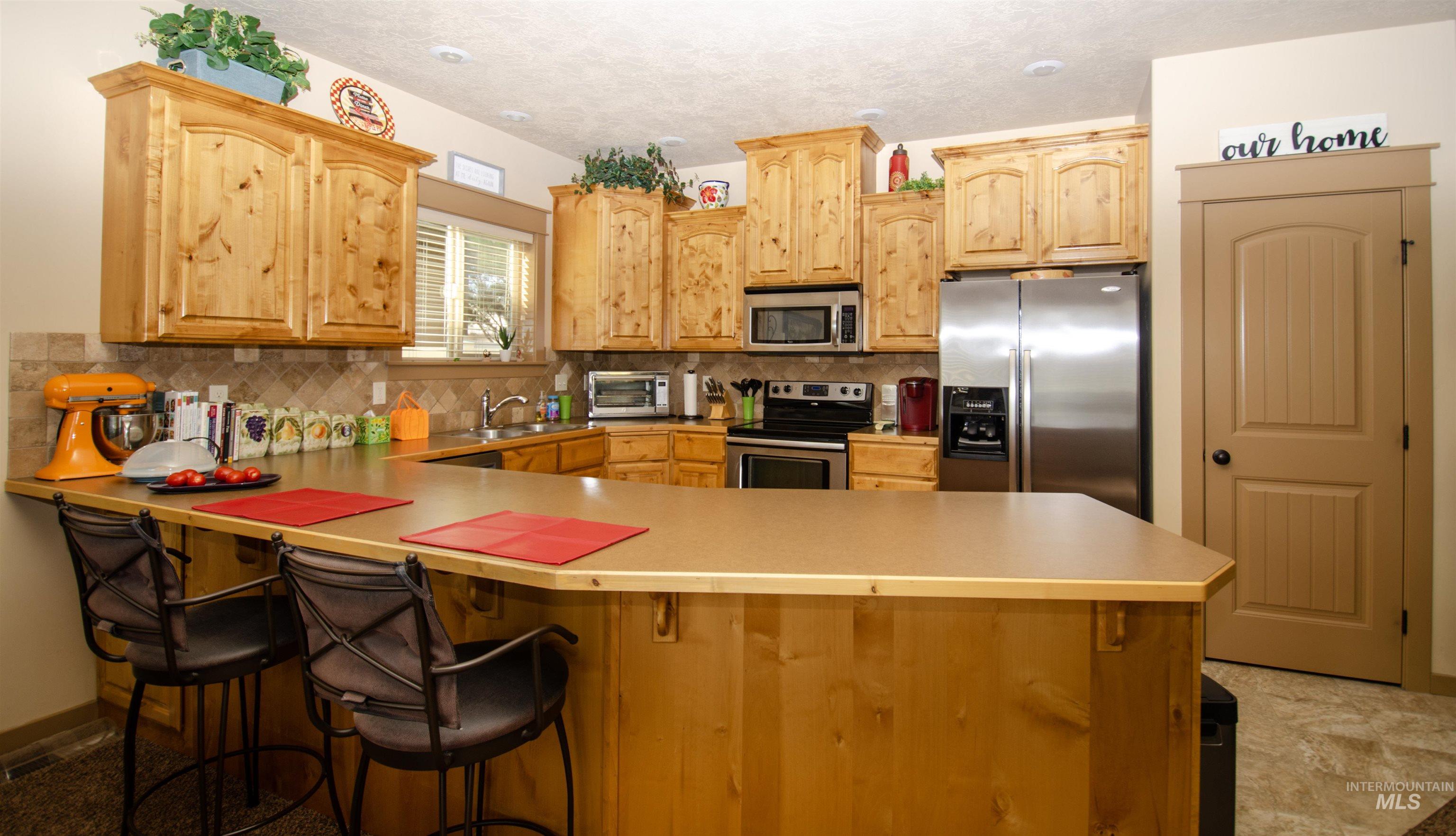 Kitchen featuring stainless steel appliances, decorative backsplash, a peninsula, light countertops, and a textured ceiling