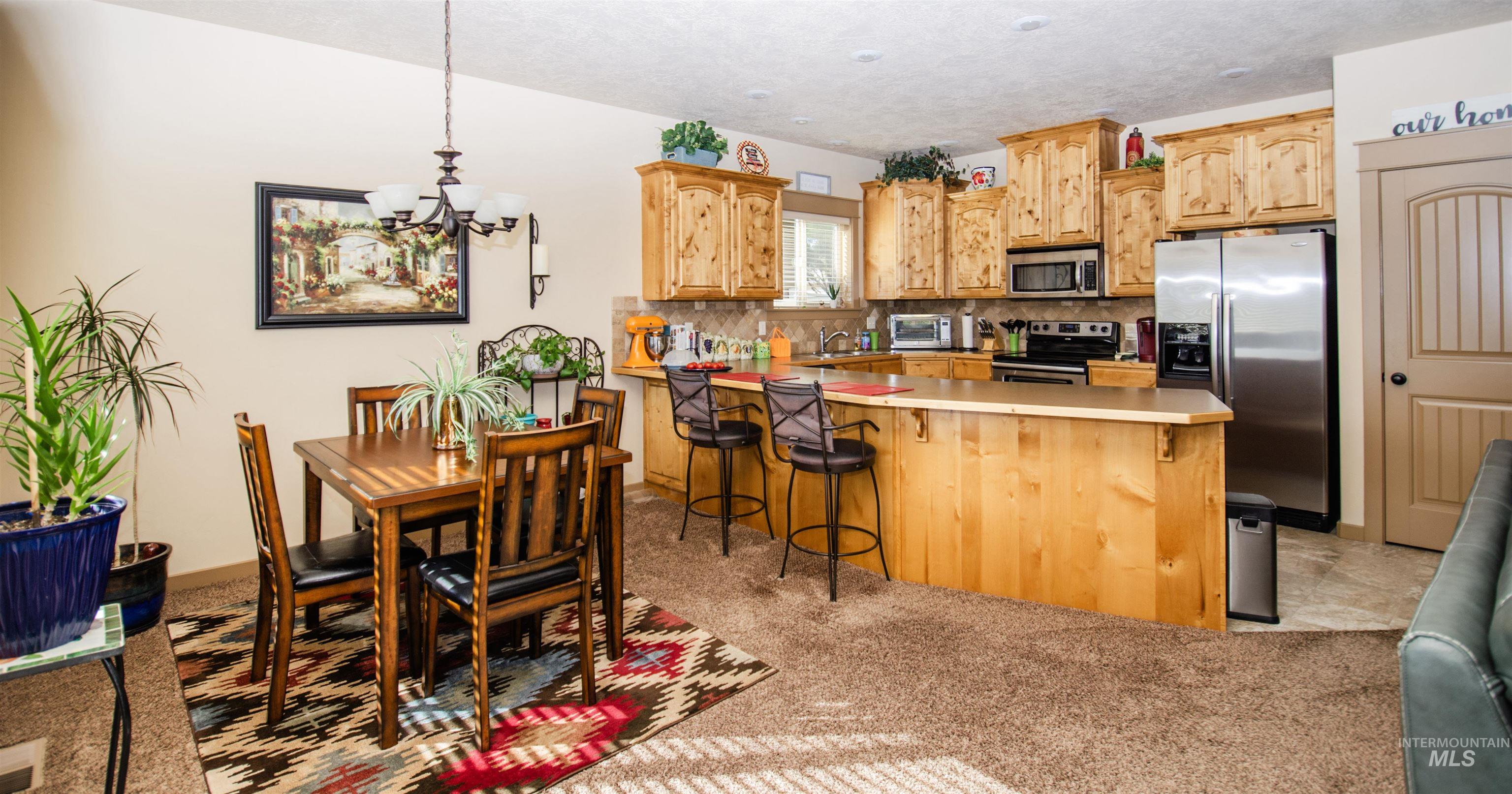 Kitchen with stainless steel appliances, a peninsula, light countertops, backsplash, and hanging light fixtures