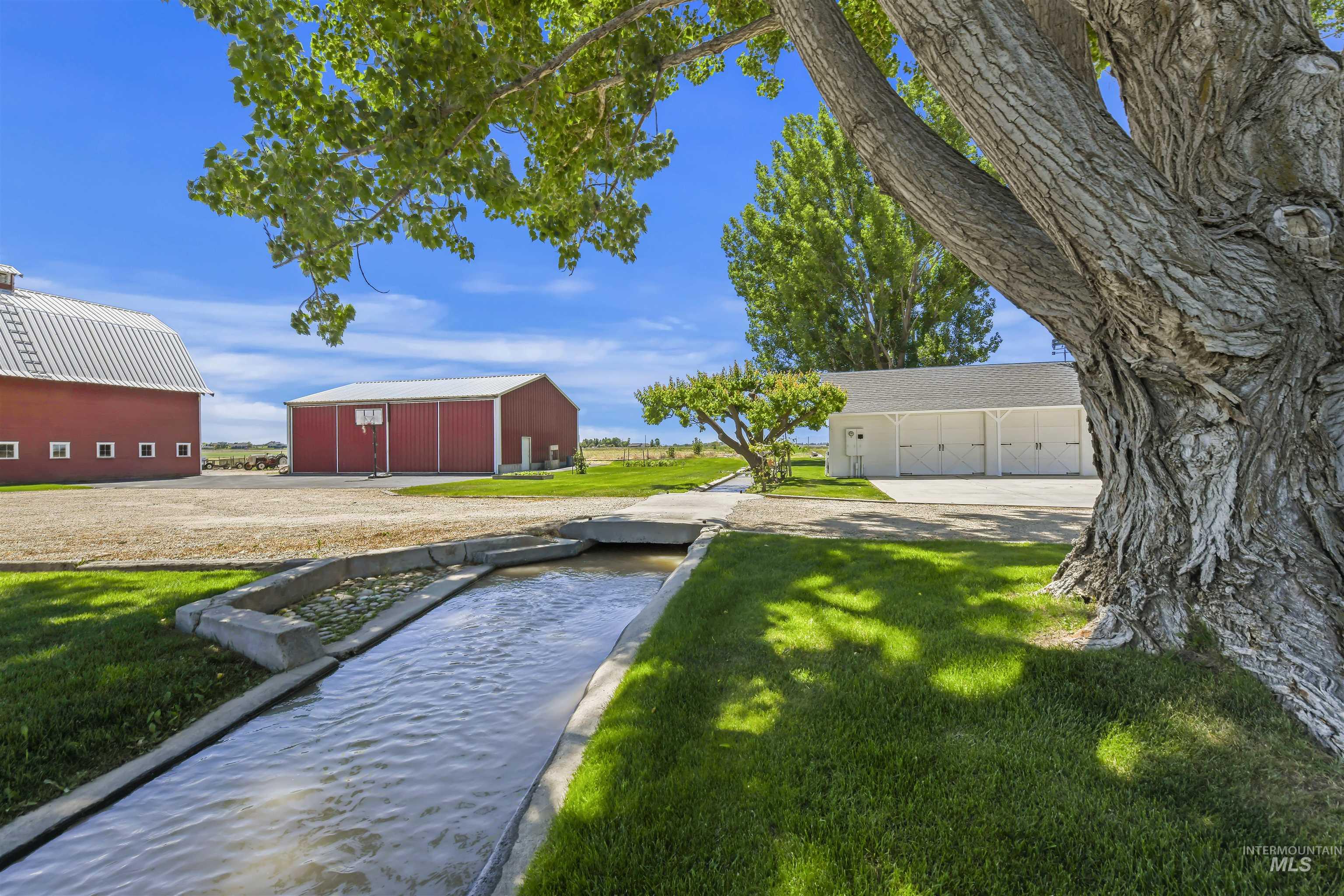 View of green lawn featuring an outdoor structure, a pole building, a detached garage, and driveway