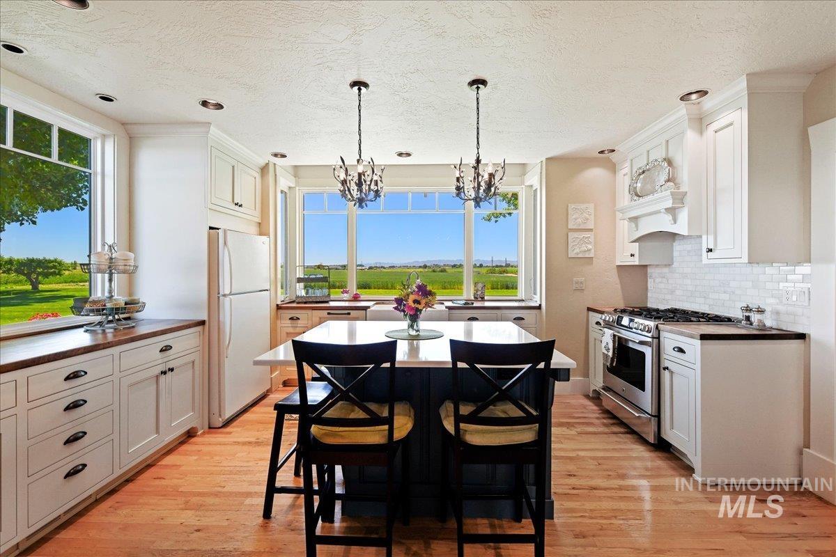 Kitchen with gas range, freestanding refrigerator, light wood-type flooring, decorative backsplash, and a textured ceiling