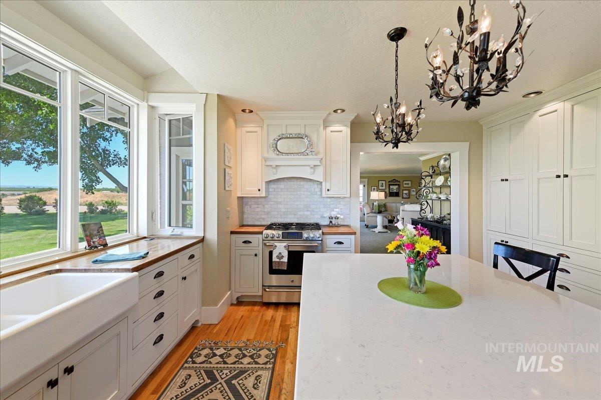 Kitchen with gas stove, decorative light fixtures, white cabinetry, light wood-style flooring, and backsplash