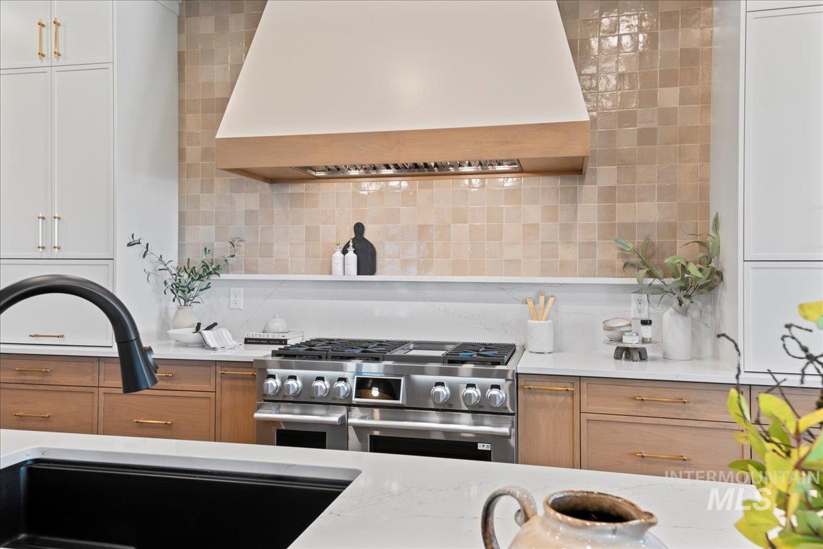 Kitchen with custom range hood, light stone counters, range with two ovens, and designer backsplash