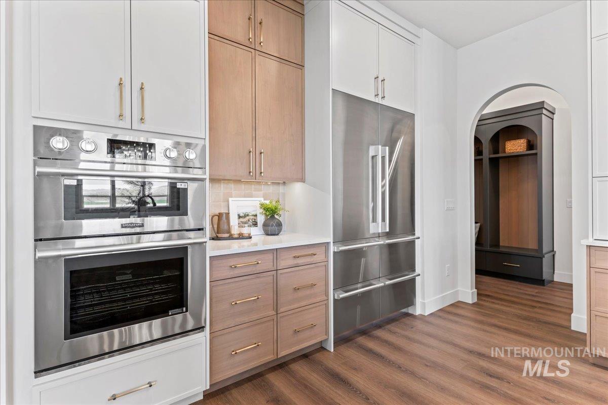 Kitchen with appliances with stainless steel finishes, decorative backsplash, dark wood-style flooring, light quartz countertops, and painted cabinets