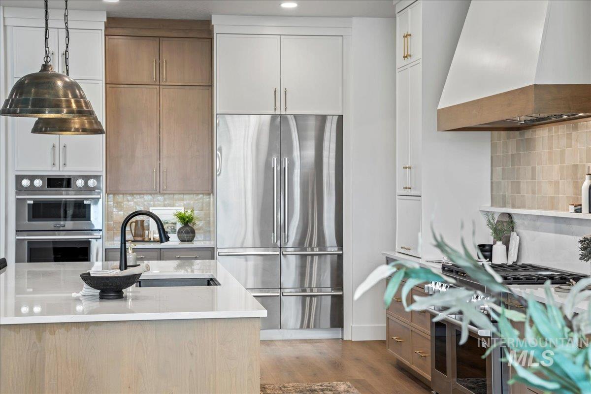 Kitchen with backsplash, custom exhaust hood, premium SKS appliances, wood finished floors, and pre-finished cabinets
