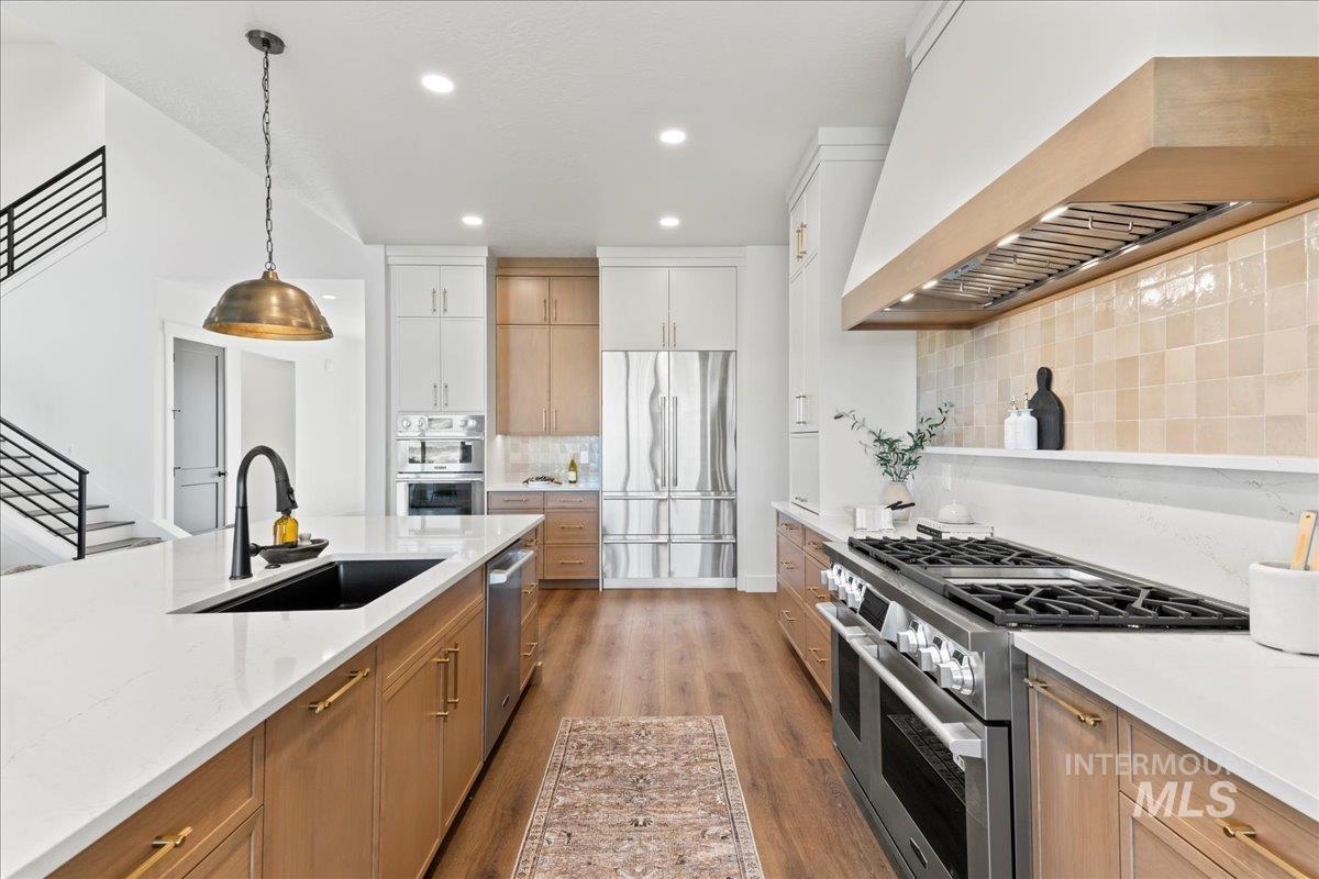 Kitchen featuring premium SKS appliances, custom exhaust hood, decorative light fixtures, light wood-type flooring, and painted cabinets