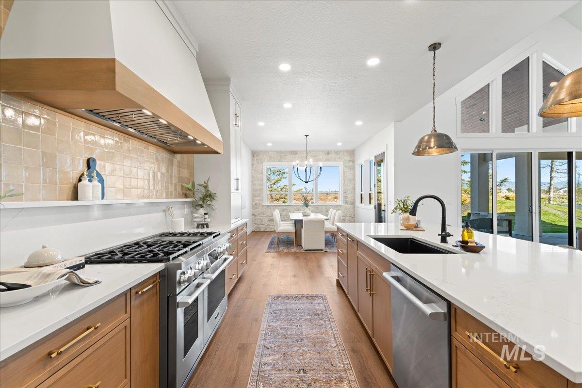 Kitchen featuring premium range hood, appliances with stainless steel finishes, pre-finshded cabinetry, light wood-style flooring, and hanging light fixtures