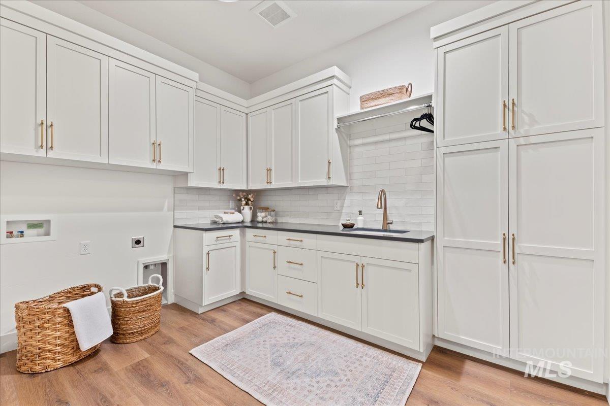 Laundry area with light wood-type flooring, hookup for an electric dryer, cabinet space, and hookup for a washing machine