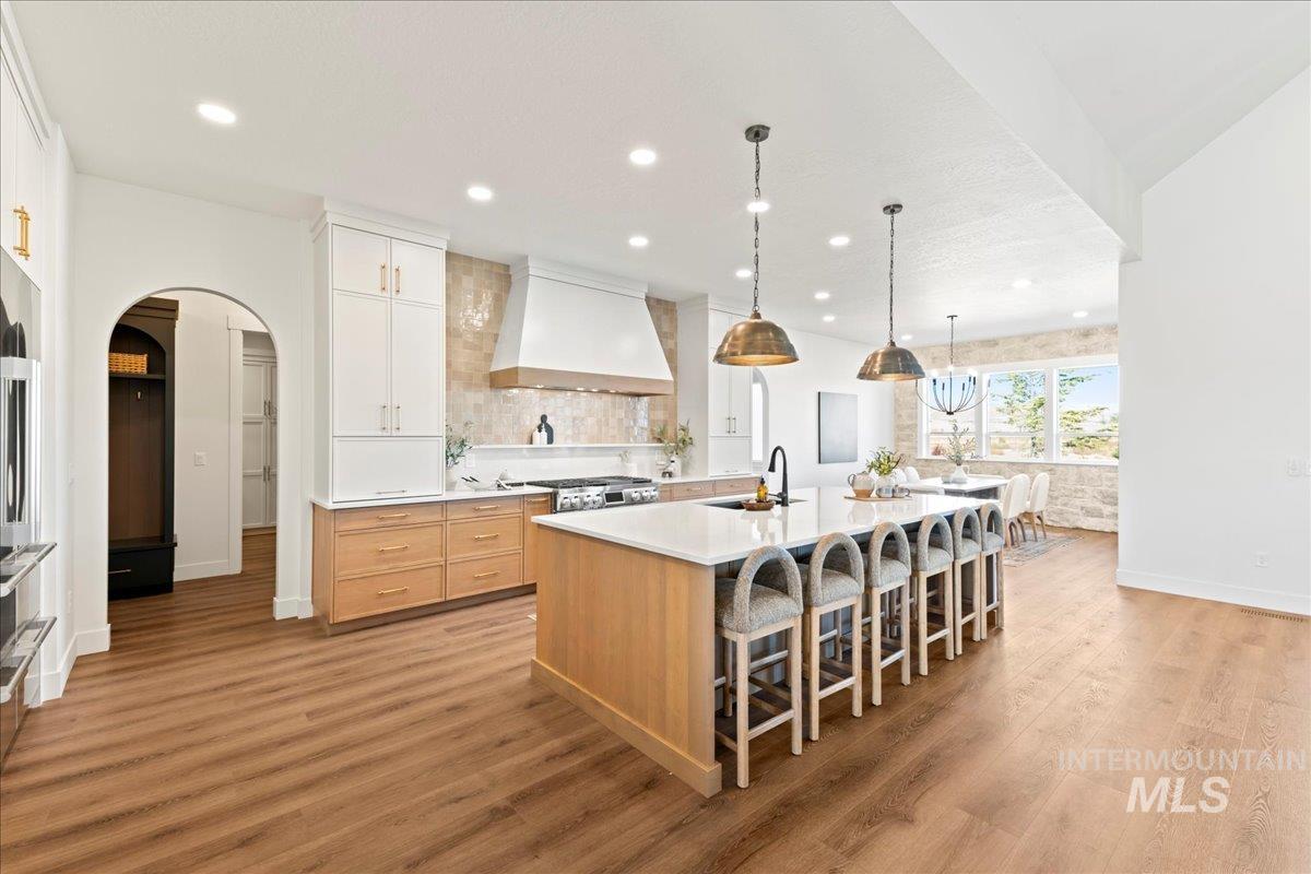 Kitchen with a large island with sink, arched walkways, pendant lighting, a breakfast bar area, and light wood-style floors