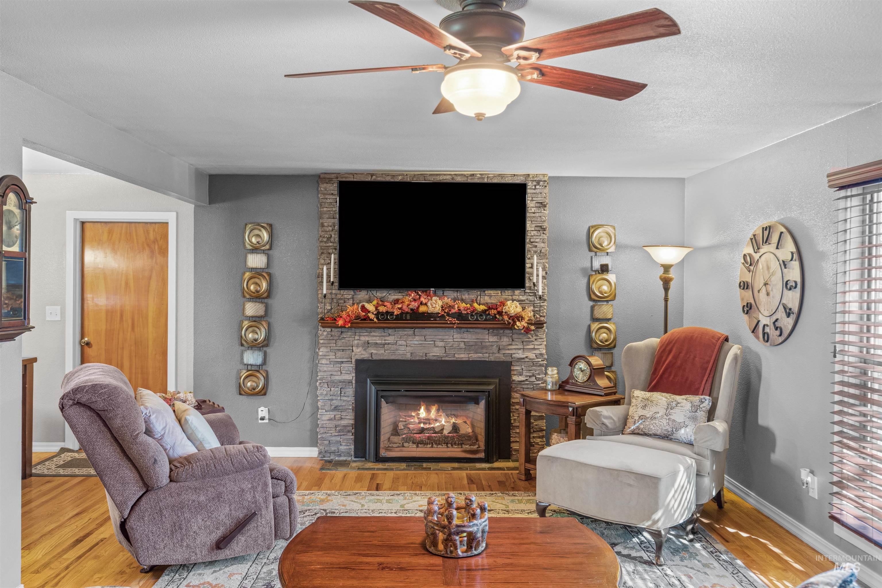 Living area featuring a gas fireplace, wood finished floors, ceiling fan, and a textured ceiling