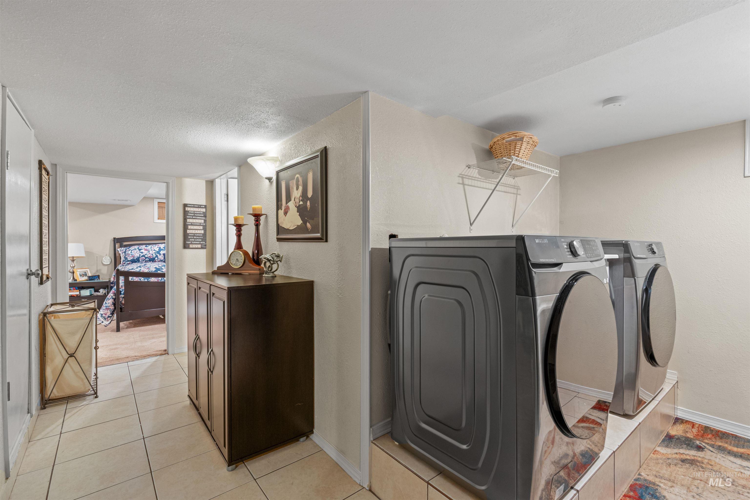 Washroom featuring light tile patterned floors, washing machine and clothes dryer, a textured ceiling, and a textured wall