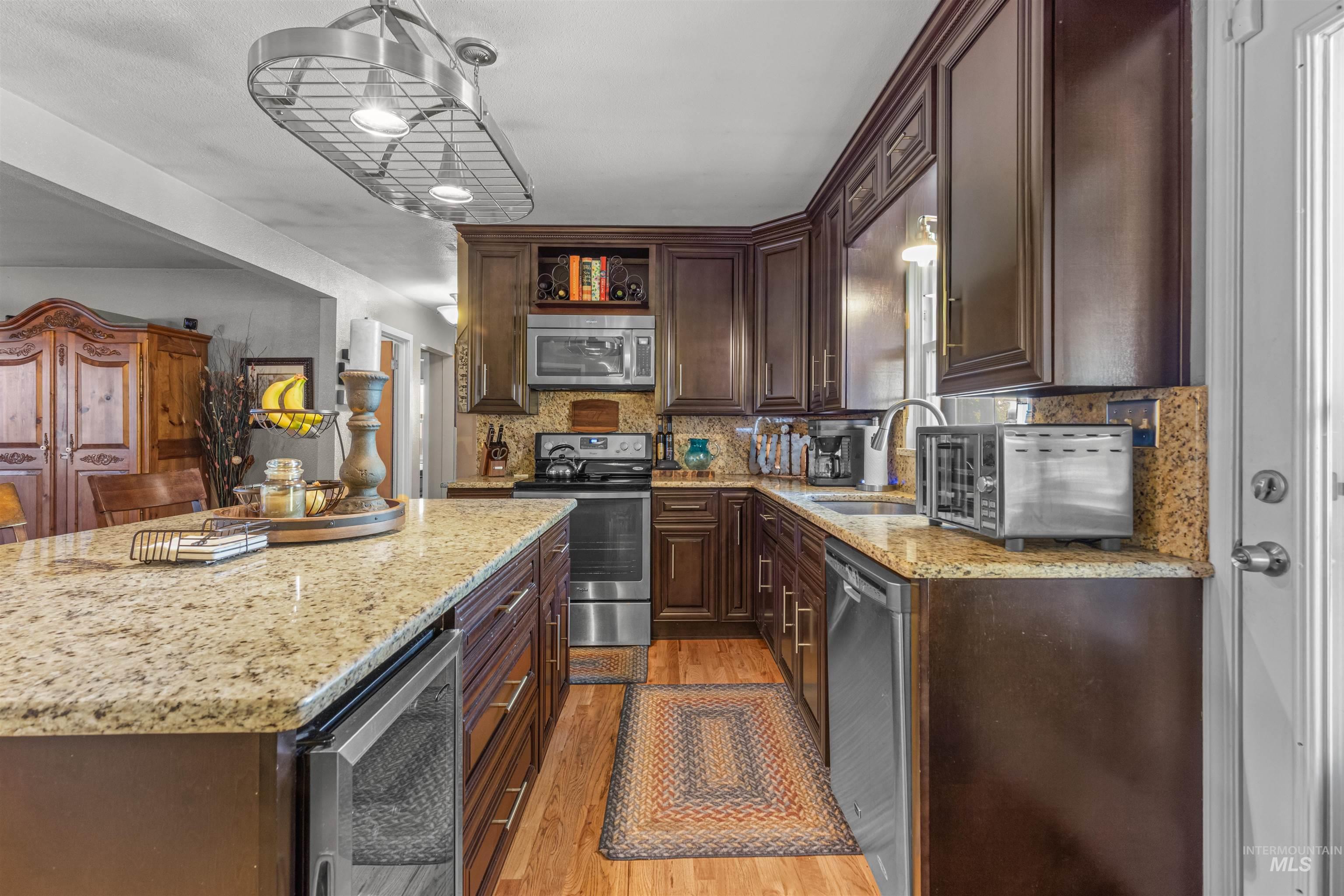 Kitchen featuring dark brown cabinetry, stainless steel appliances, light wood-style floors, Granite countertops, and tasteful backsplash