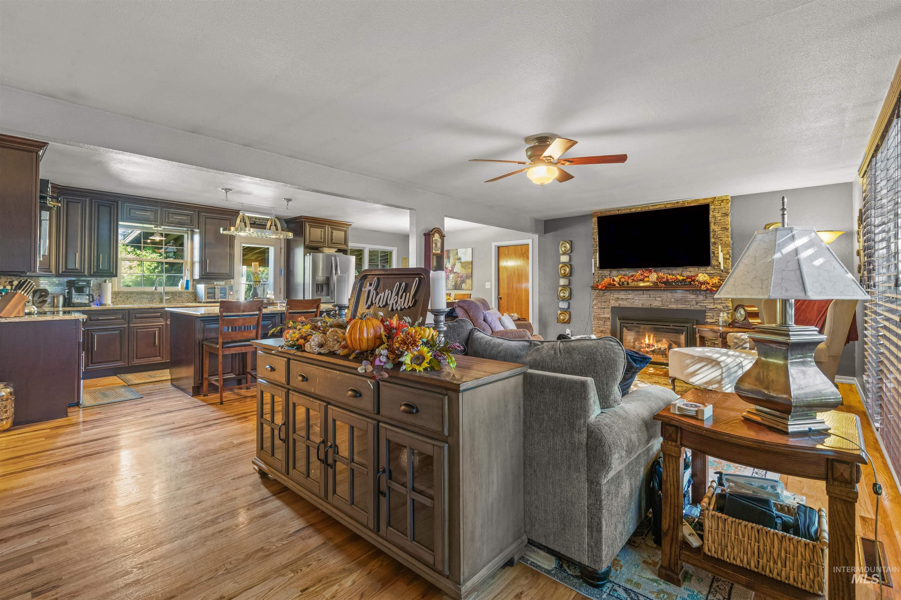 Living room featuring light wood-style floors, a fireplace, a ceiling fan, and a textured ceiling