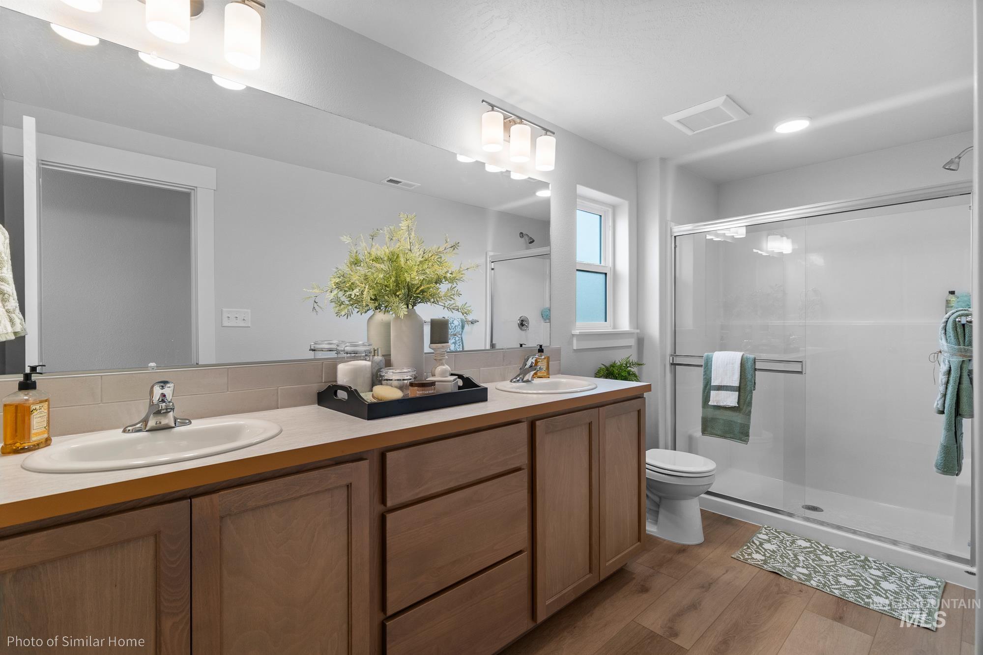 Full bathroom featuring a shower stall, double vanity, and light wood-style flooring