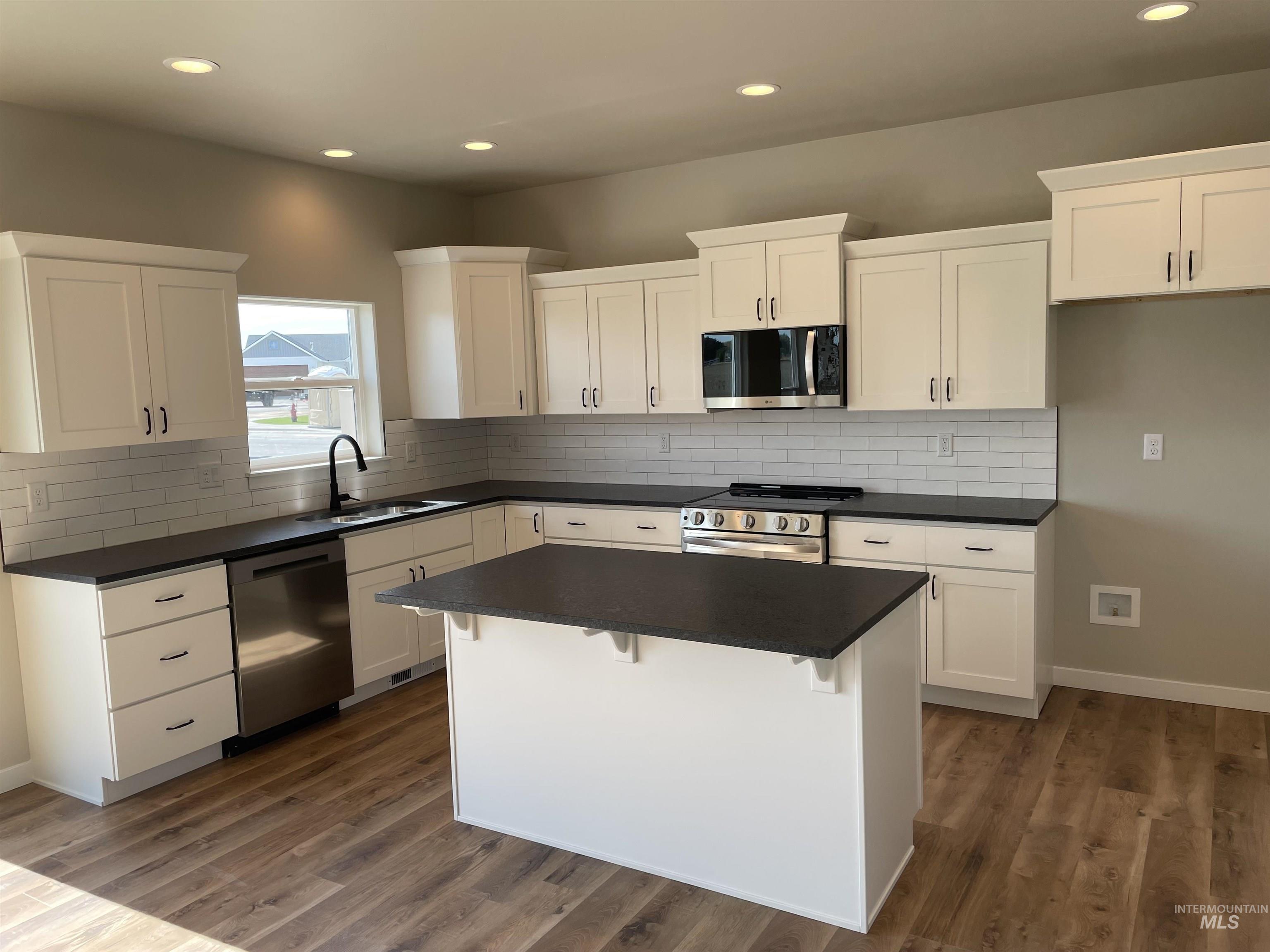 Kitchen featuring white cabinets, recessed lighting, appliances with stainless steel finishes, a kitchen bar, and a center island