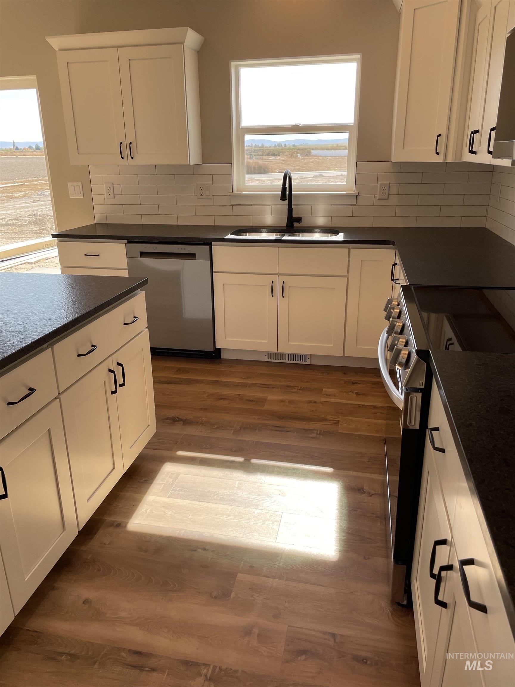 Kitchen with stainless steel appliances, white cabinets, dark wood-style flooring, and dark stone counters