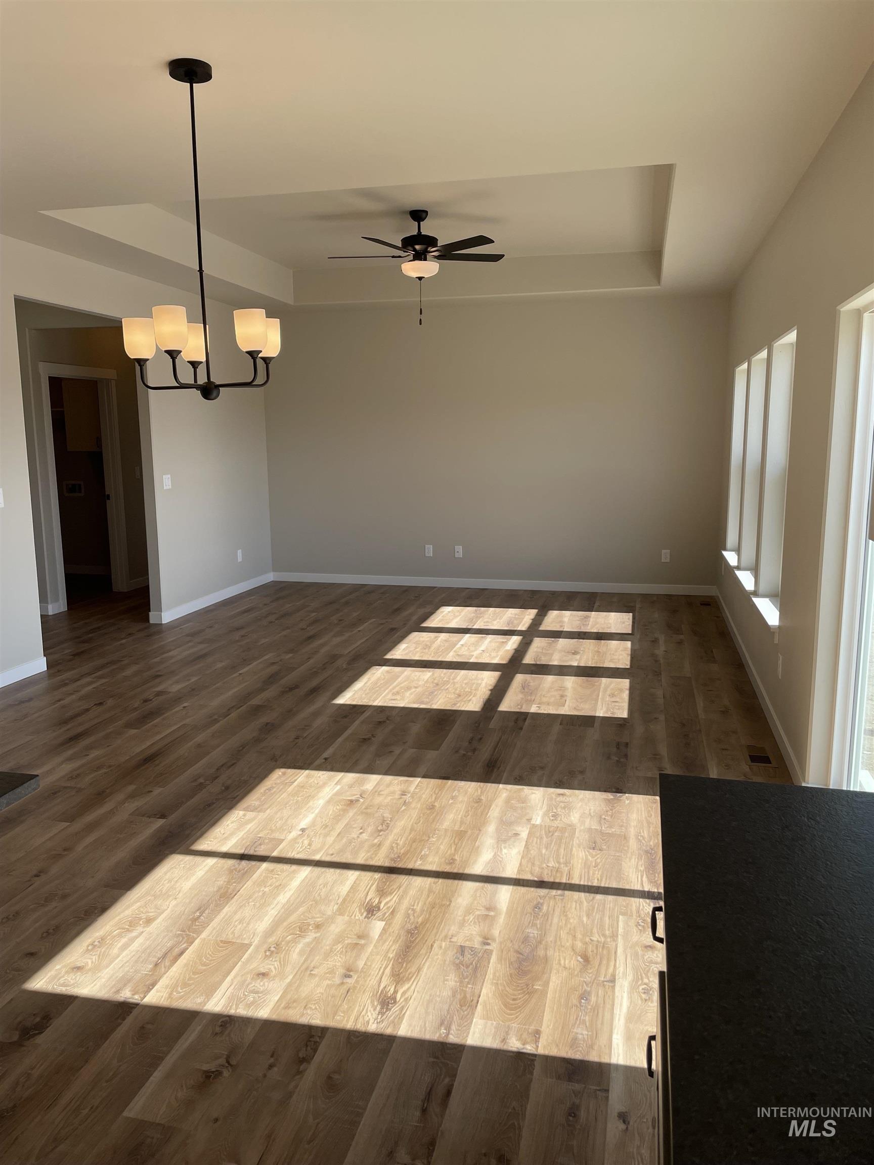 Unfurnished living room with a raised ceiling, dark wood-style floors, and a ceiling fan