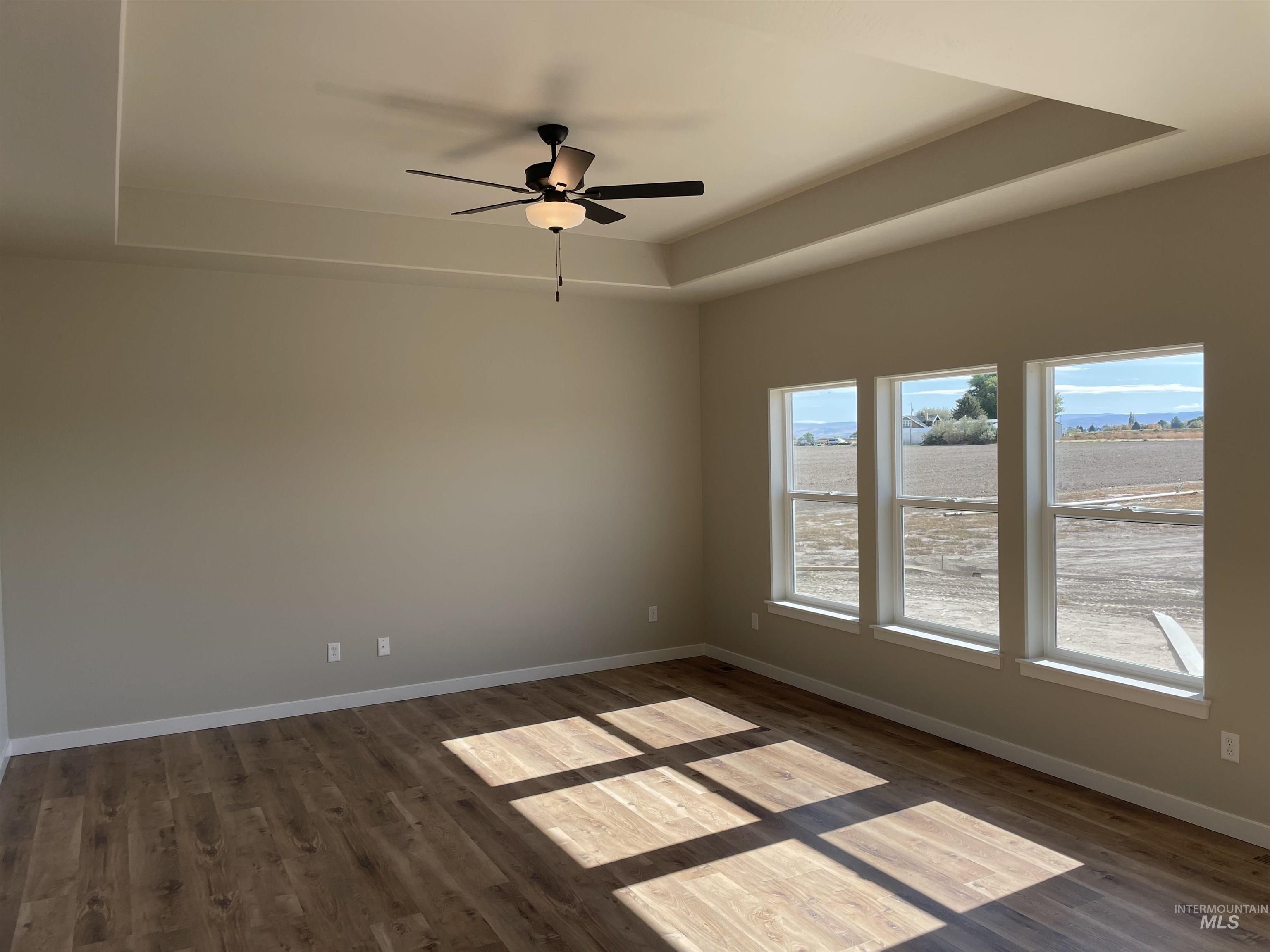 Spare room featuring a raised ceiling, dark wood-style floors, and a ceiling fan