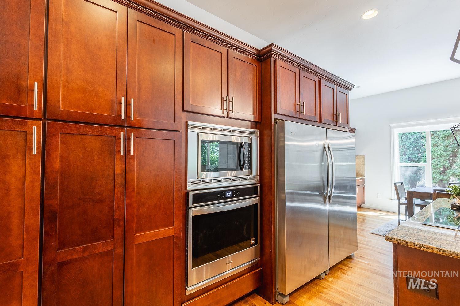 Kitchen featuring appliances with stainless steel finishes, light wood-type flooring, light stone countertops, recessed lighting, and brown cabinets
