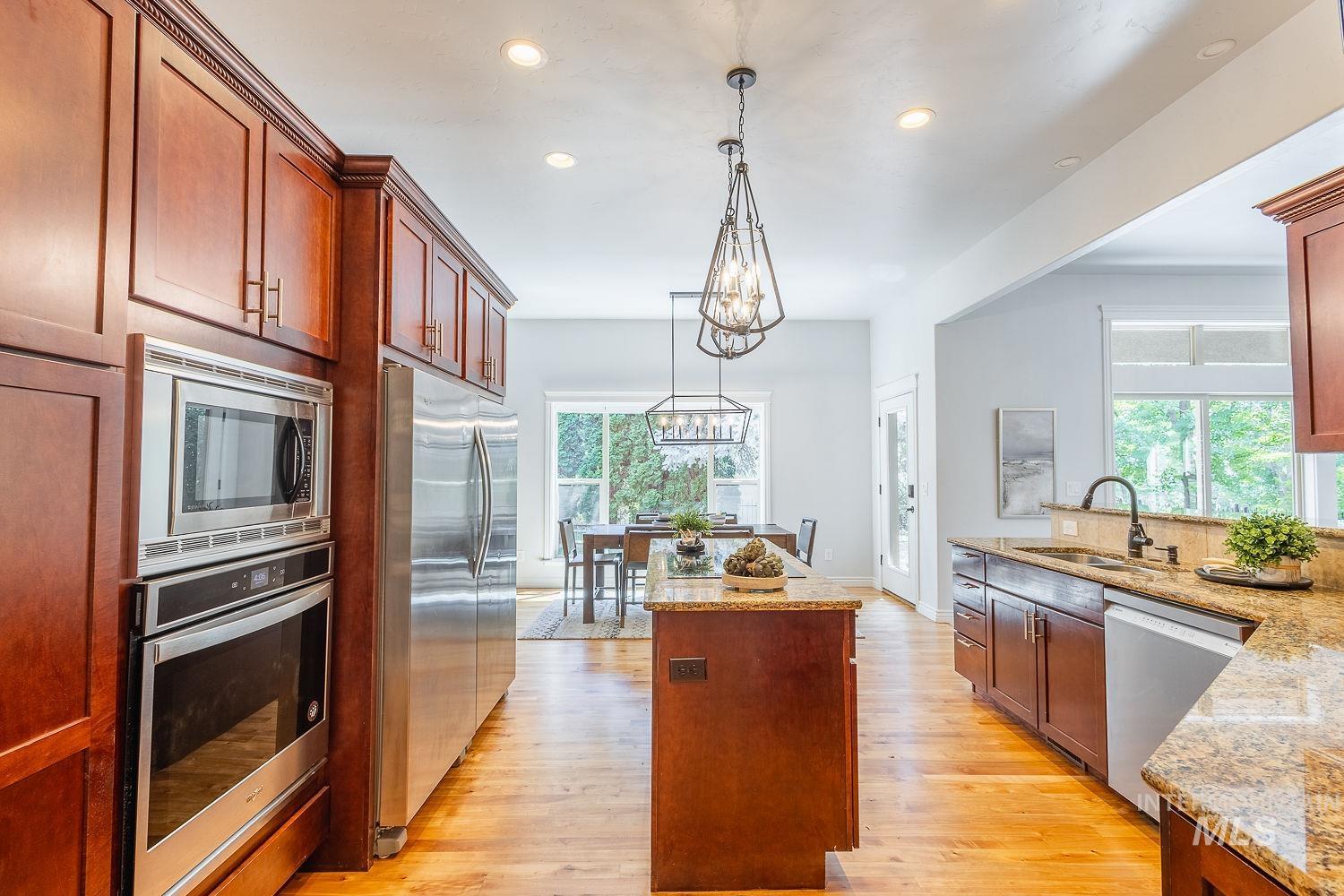 Kitchen featuring a center island, stainless steel appliances, light wood-style floors, light stone counters, and pendant lighting