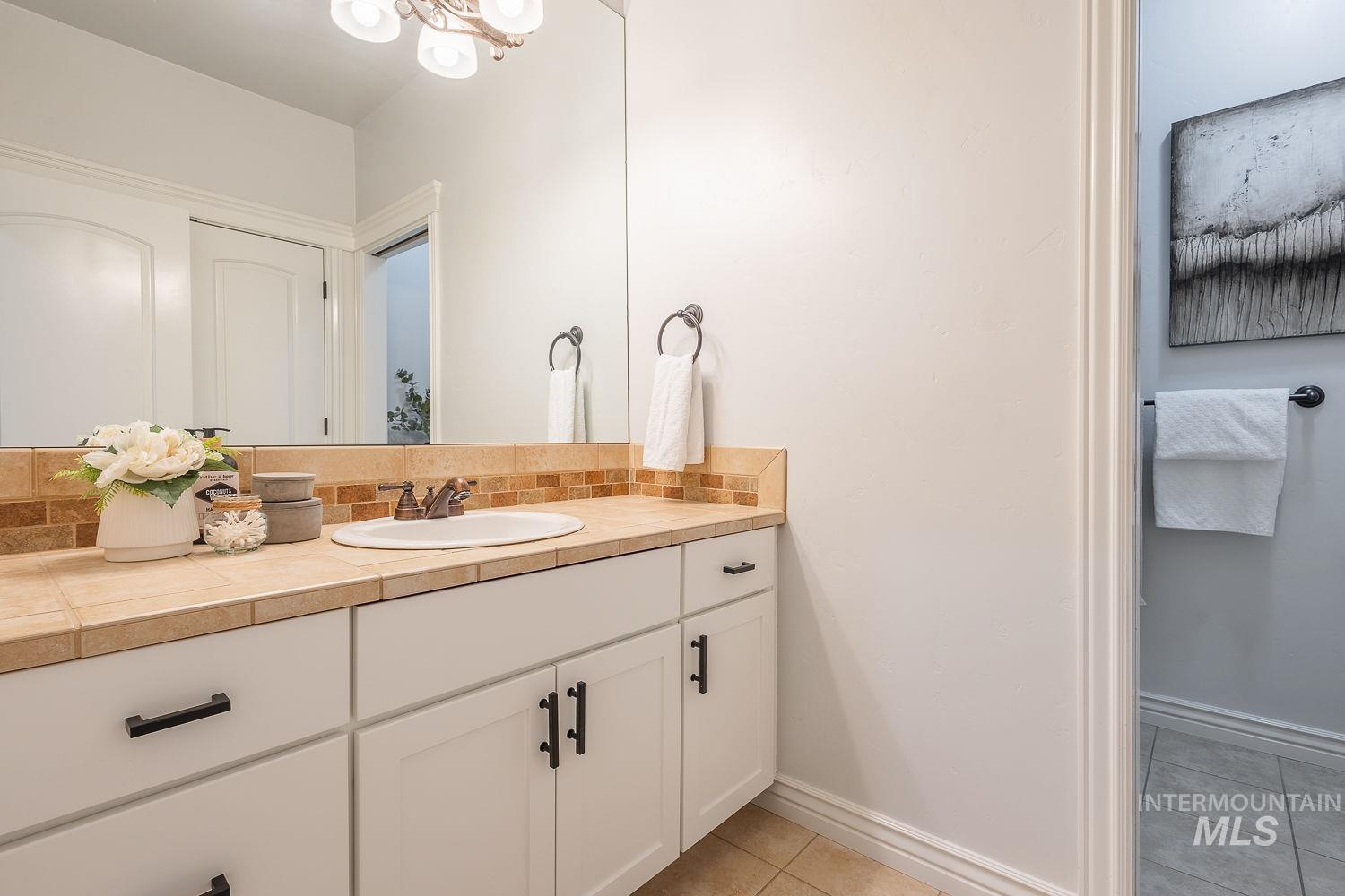 Bathroom with vanity, light tile patterned flooring, tasteful backsplash, and a chandelier