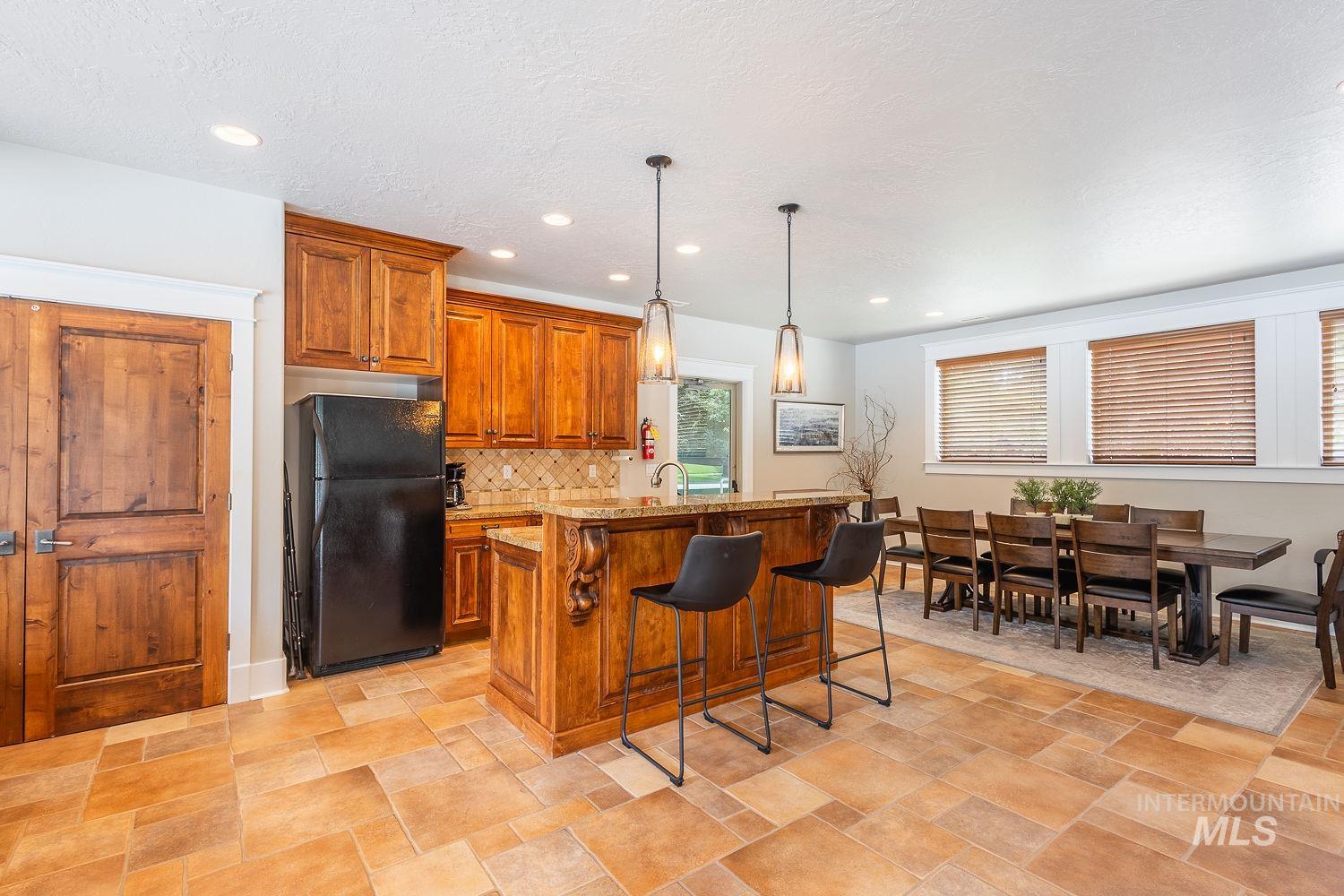 Kitchen featuring brown cabinets, freestanding refrigerator, pendant lighting, a kitchen island with sink, and a breakfast bar area