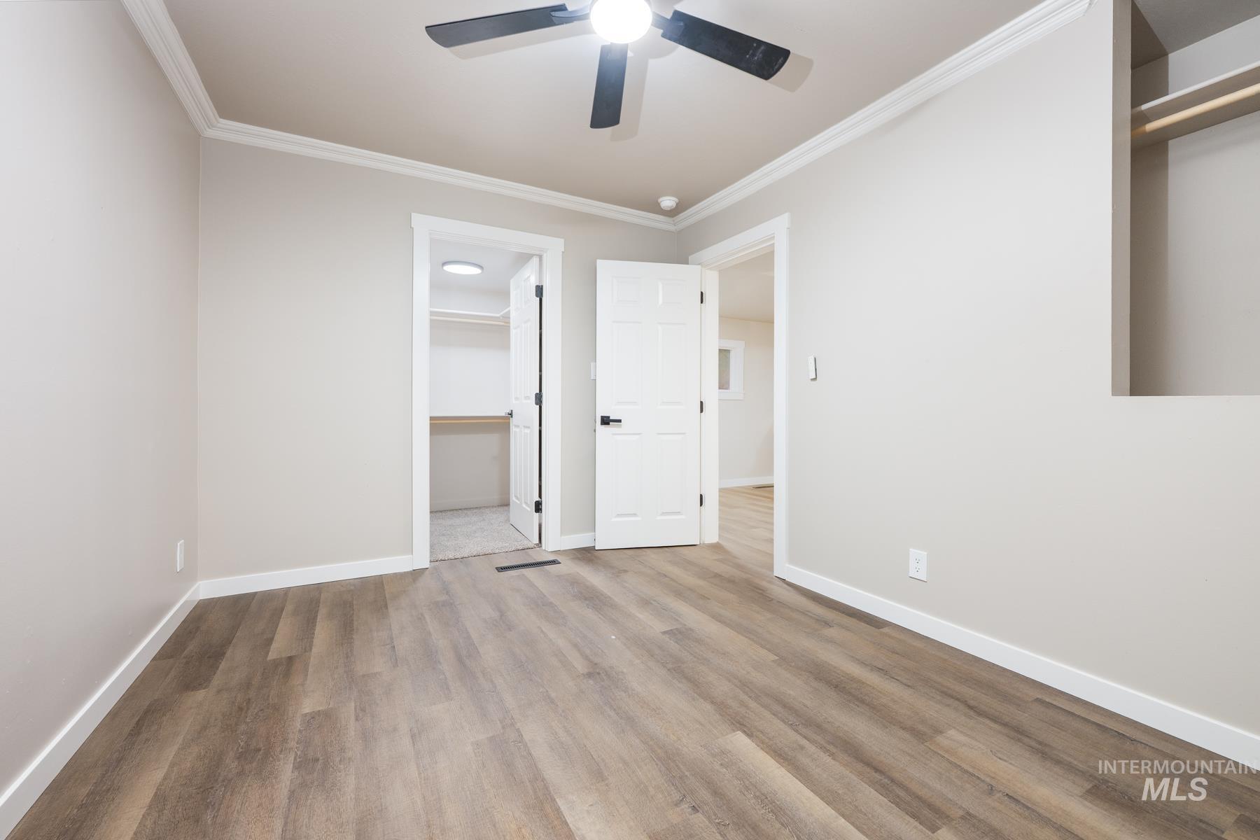 Unfurnished bedroom with ornamental molding, a walk in closet, wood finished floors, and a ceiling fan