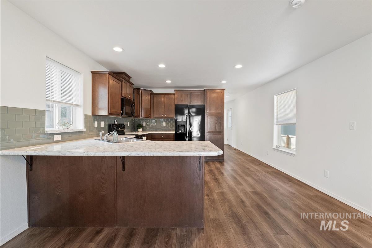 Kitchen with black appliances, backsplash, a kitchen bar, dark brown cabinetry, and a peninsula