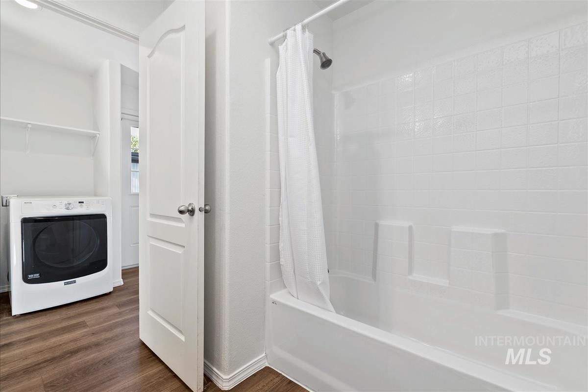 Bathroom with washer / dryer, dark wood-style floors, and shower / bathtub combination with curtain
