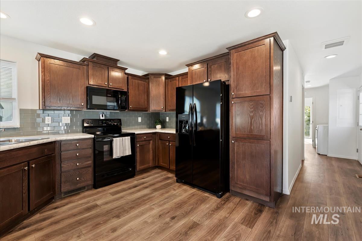 Kitchen with black appliances, decorative backsplash, recessed lighting, dark brown cabinetry, and light wood-style flooring