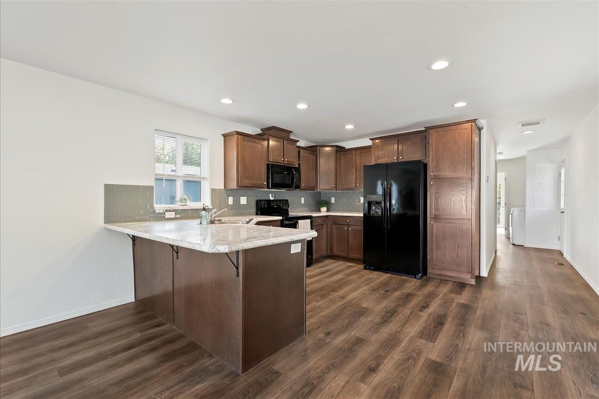 Kitchen featuring a peninsula, black appliances, a breakfast bar, decorative backsplash, and dark brown cabinets