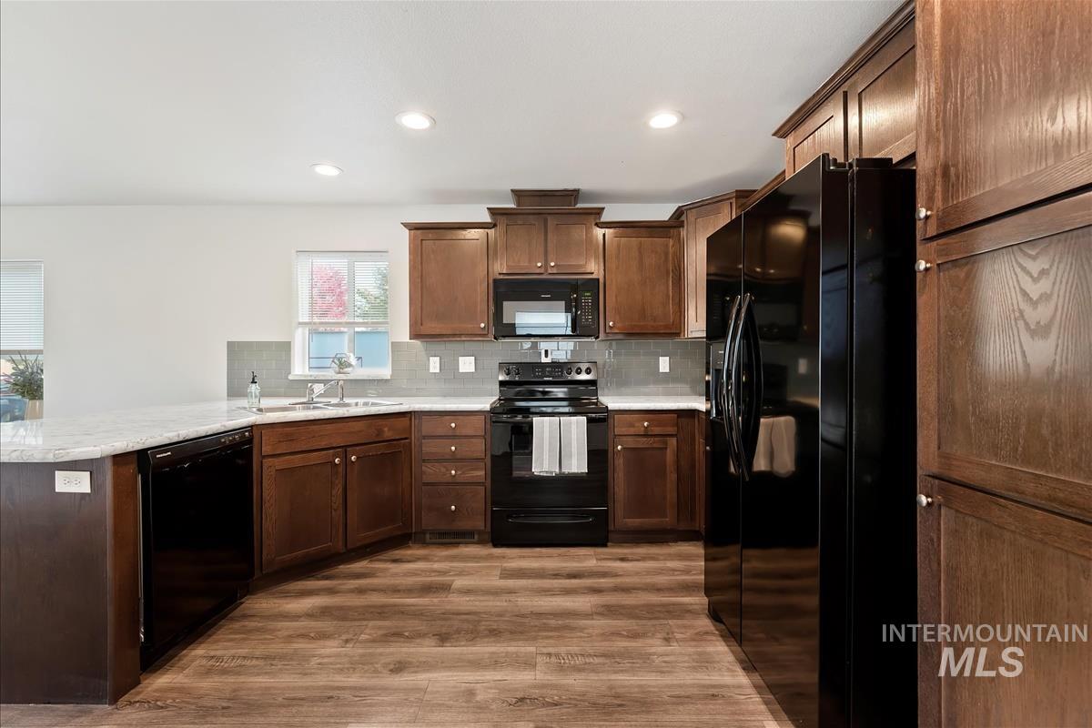 Kitchen with black appliances, tasteful backsplash, light wood-style floors, recessed lighting, and a peninsula