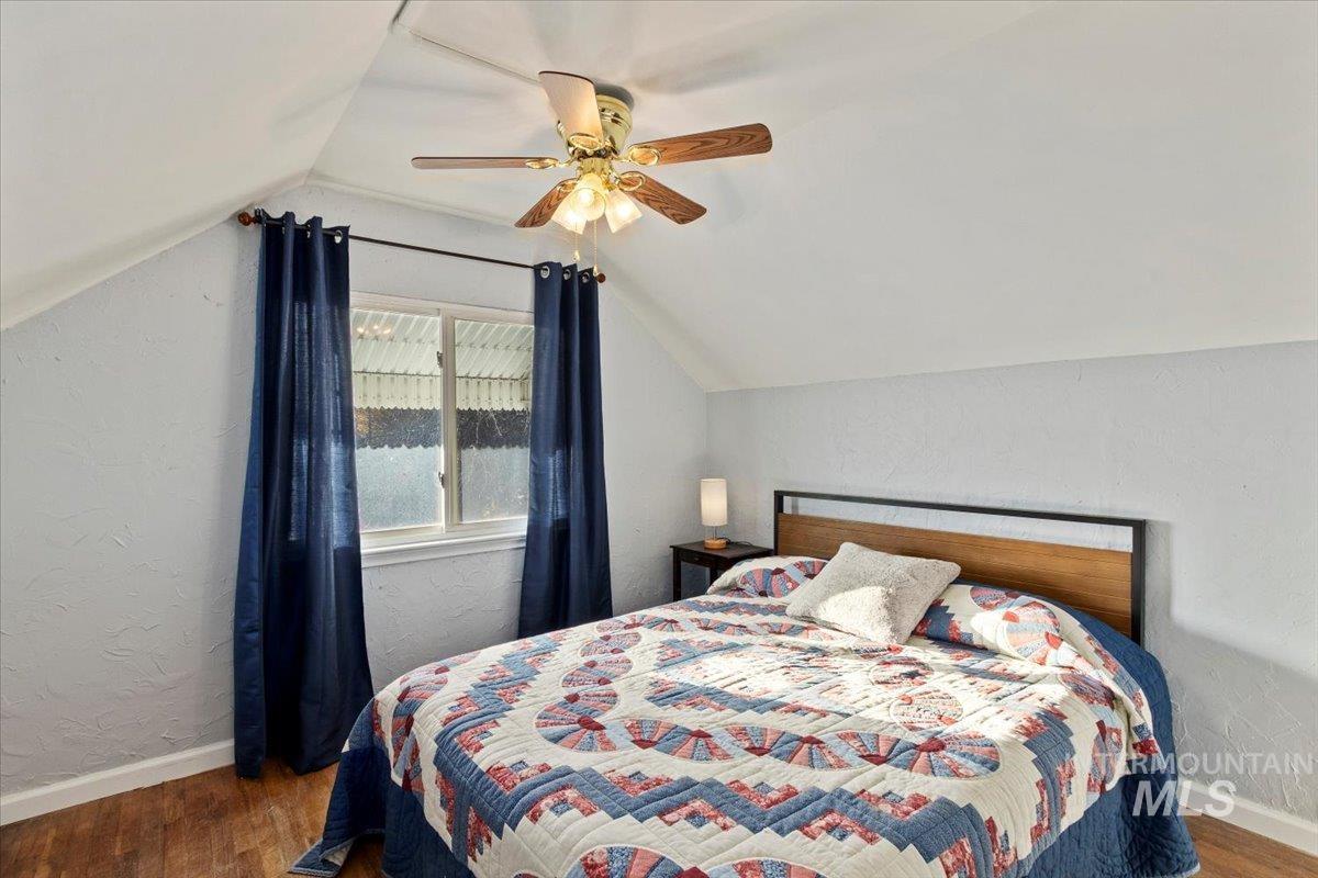 Bedroom featuring a textured wall, dark wood-style floors, vaulted ceiling, and a ceiling fan