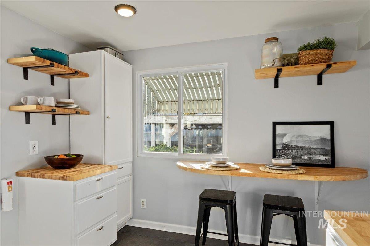 Kitchen with open shelves, butcher block counters, white cabinetry, and a breakfast bar area