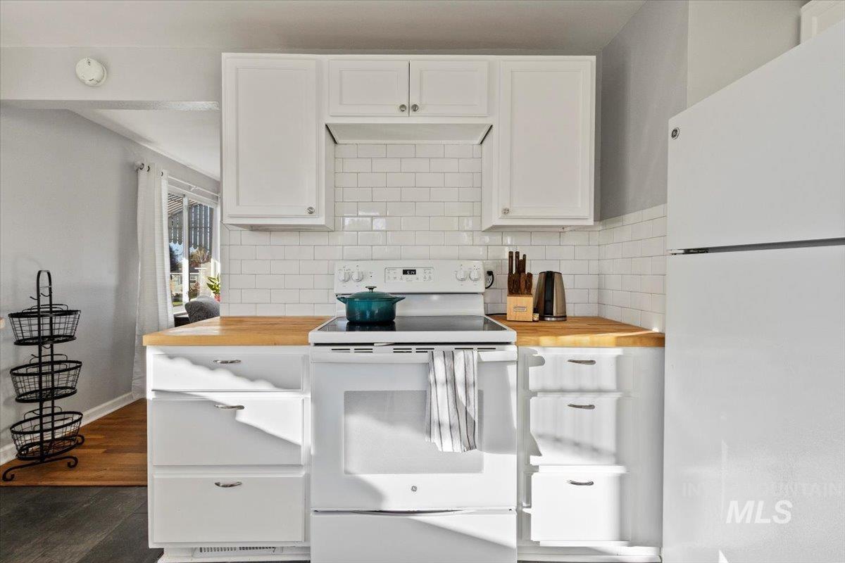 Kitchen with white appliances, wood counters, white cabinets, and tasteful backsplash