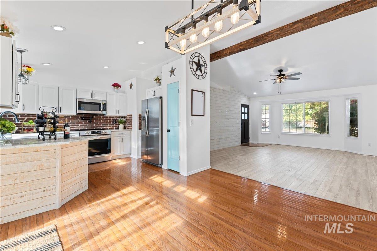 Kitchen with hanging light fixtures, open floor plan, light wood-style flooring, stainless steel appliances, and backsplash