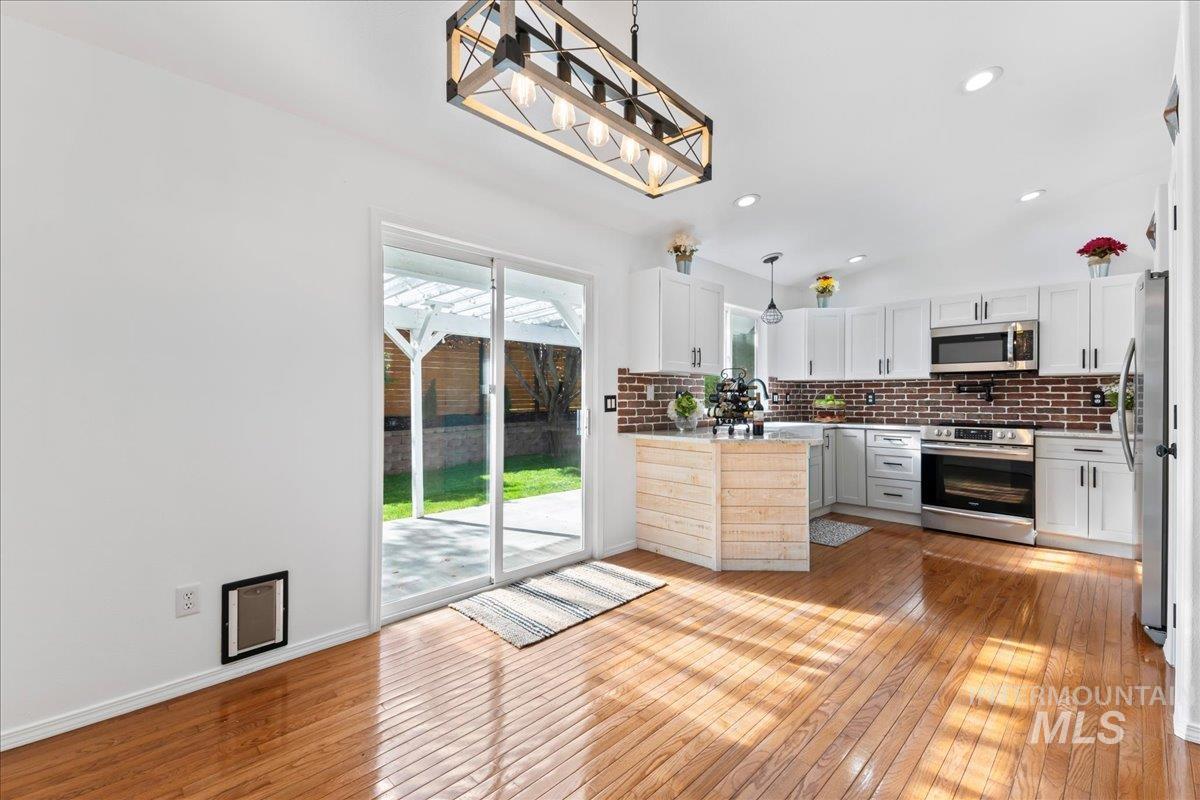 Kitchen featuring decorative light fixtures, light wood finished floors, decorative backsplash, appliances with stainless steel finishes, and white cabinetry