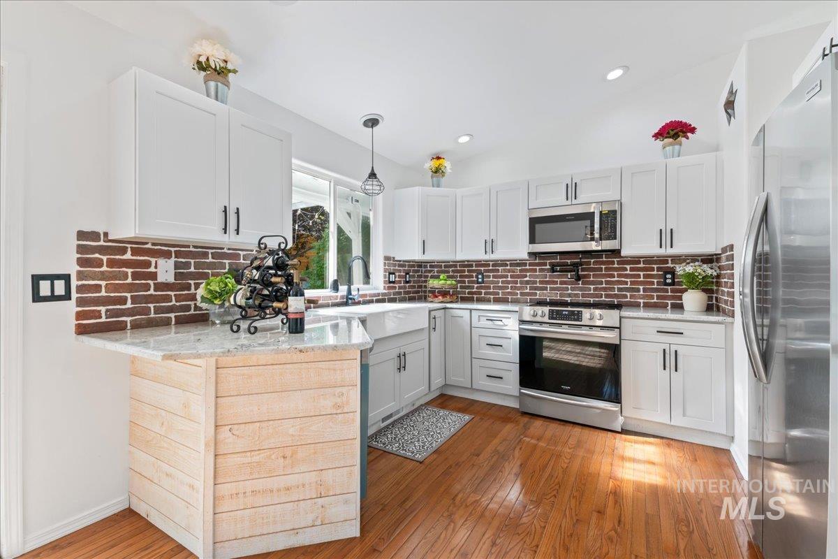 Kitchen featuring backsplash, stainless steel appliances, light stone counters, light wood-style floors, and vaulted ceiling