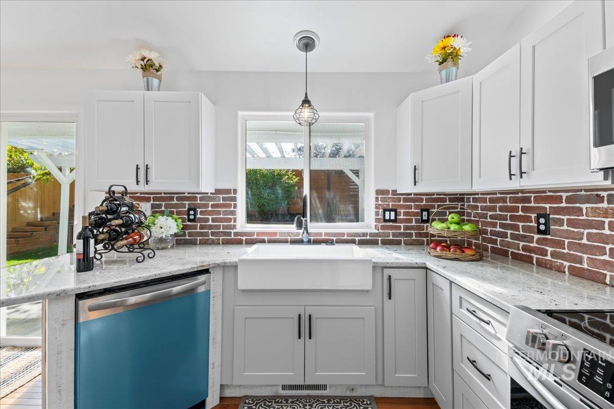 Kitchen with appliances with stainless steel finishes, light stone counters, hanging light fixtures, white cabinets, and tasteful backsplash