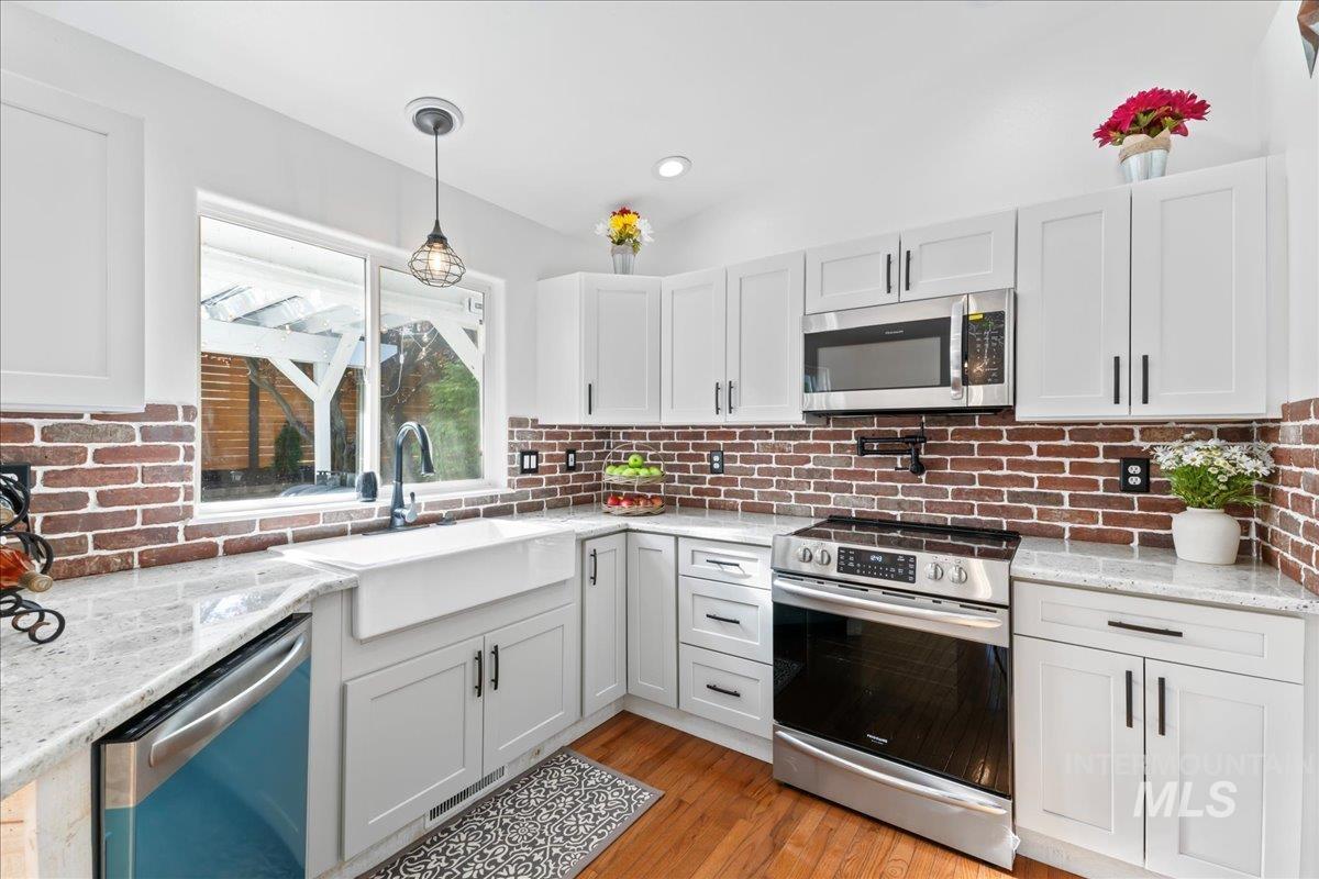 Kitchen featuring appliances with stainless steel finishes, hanging light fixtures, white cabinetry, light wood-style floors, and light stone countertops