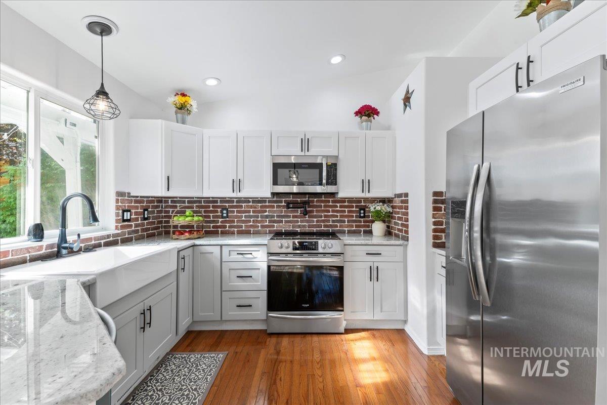 Kitchen featuring appliances with stainless steel finishes, light stone counters, pendant lighting, light wood-style flooring, and tasteful backsplash