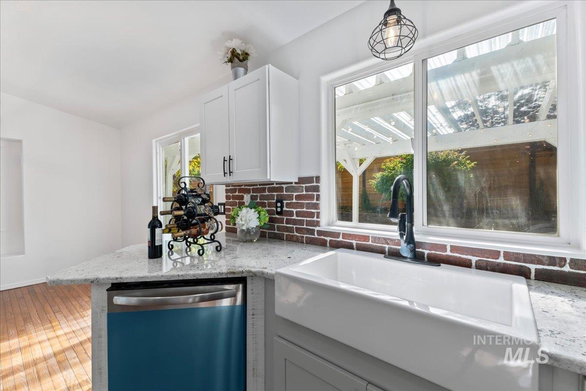 Kitchen featuring dishwasher, light stone countertops, white cabinetry, decorative backsplash, and a peninsula
