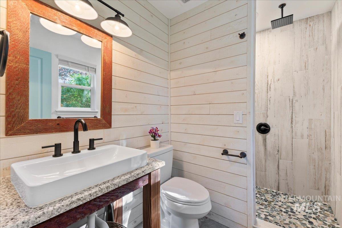 Bathroom with tiled shower, wood walls, and vanity
