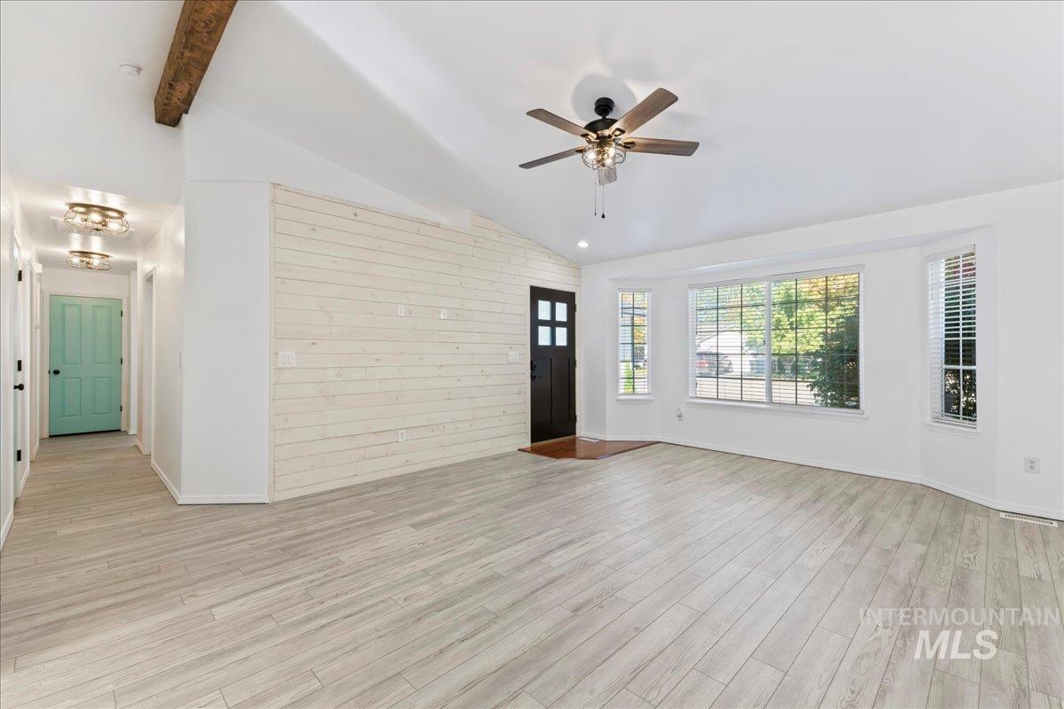 Unfurnished living room featuring light wood-style floors, ceiling fan, beam ceiling, and high vaulted ceiling