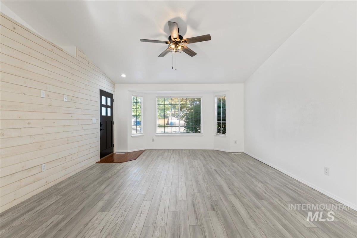 Unfurnished living room with wooden walls, light wood-style floors, a ceiling fan, and lofted ceiling