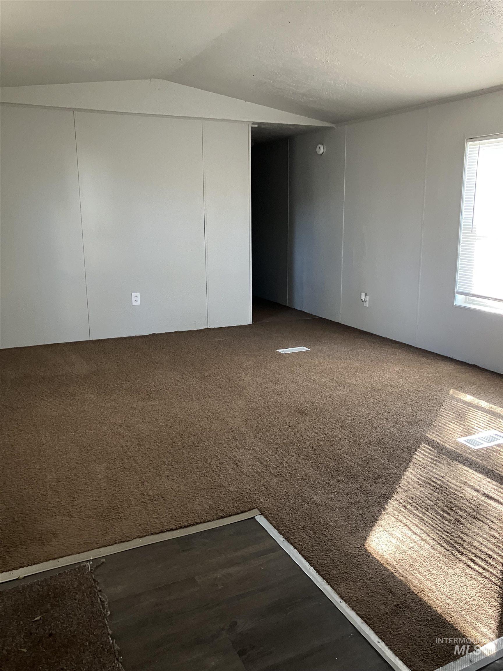 Empty room with dark carpet, a textured ceiling, dark wood finished floors, lofted ceiling, and a decorative wall