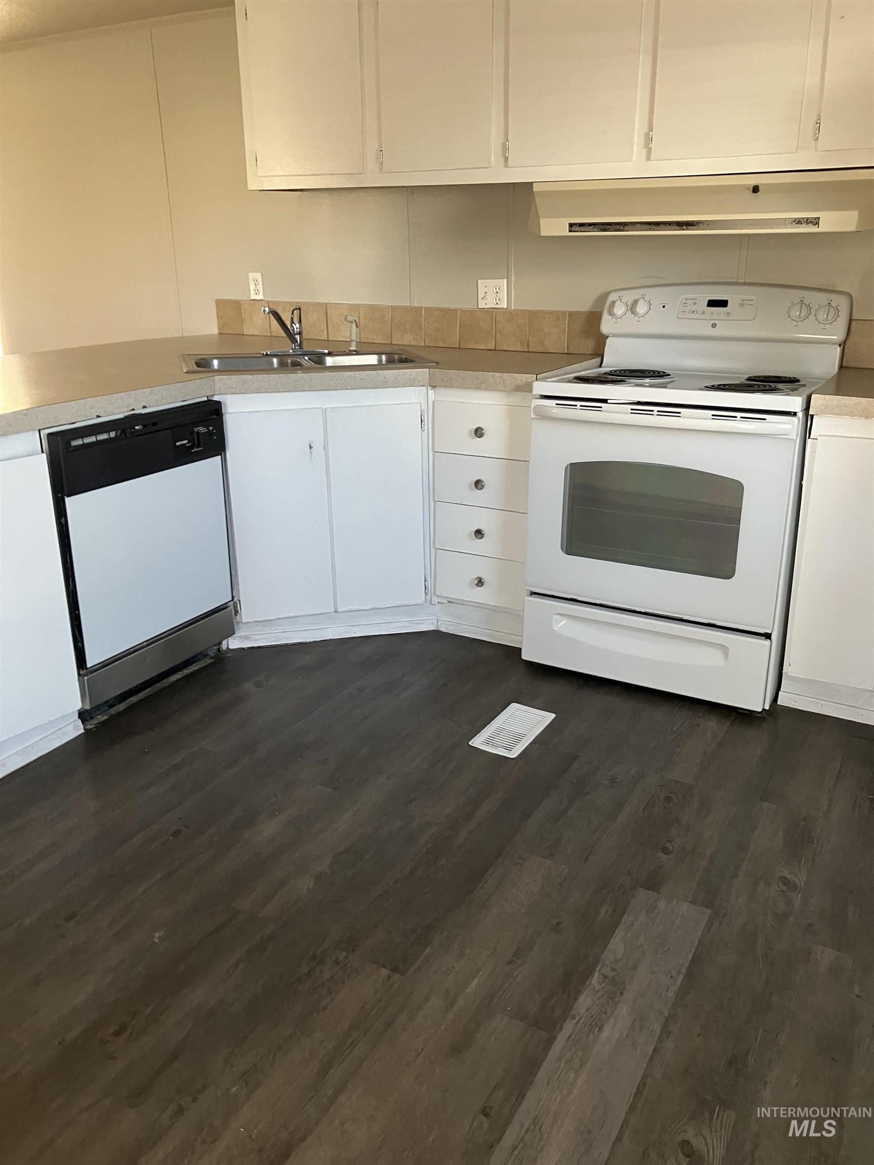 Kitchen featuring white appliances, white cabinets, light countertops, ventilation hood, and dark wood-style floors