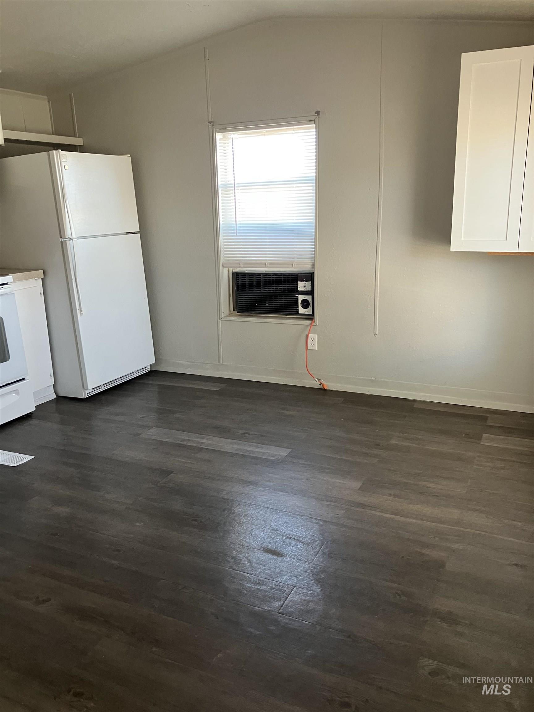 Unfurnished dining area featuring dark wood-style flooring, vaulted ceiling, and cooling unit