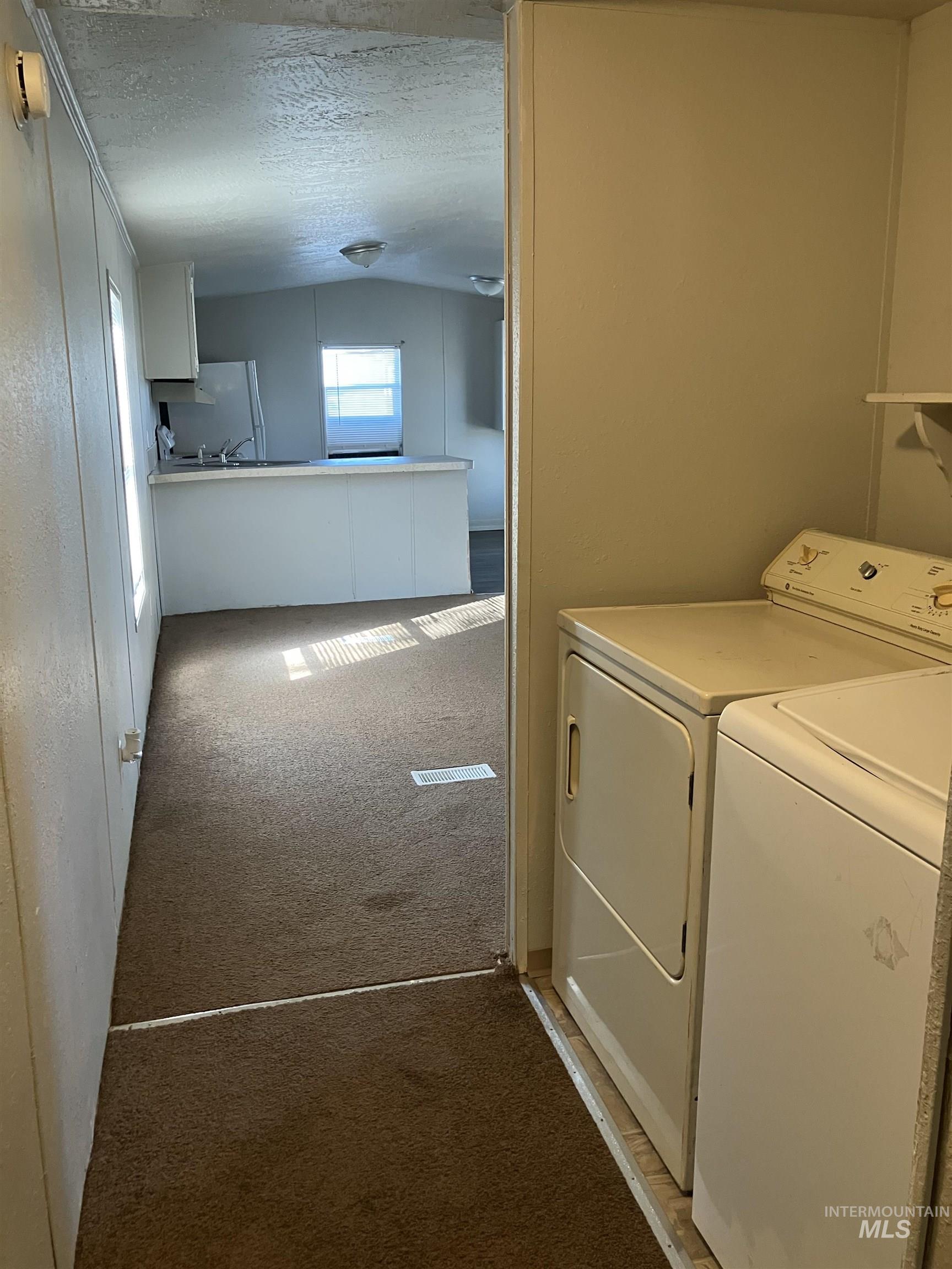 Laundry room with light colored carpet, a textured ceiling, and independent washer and dryer