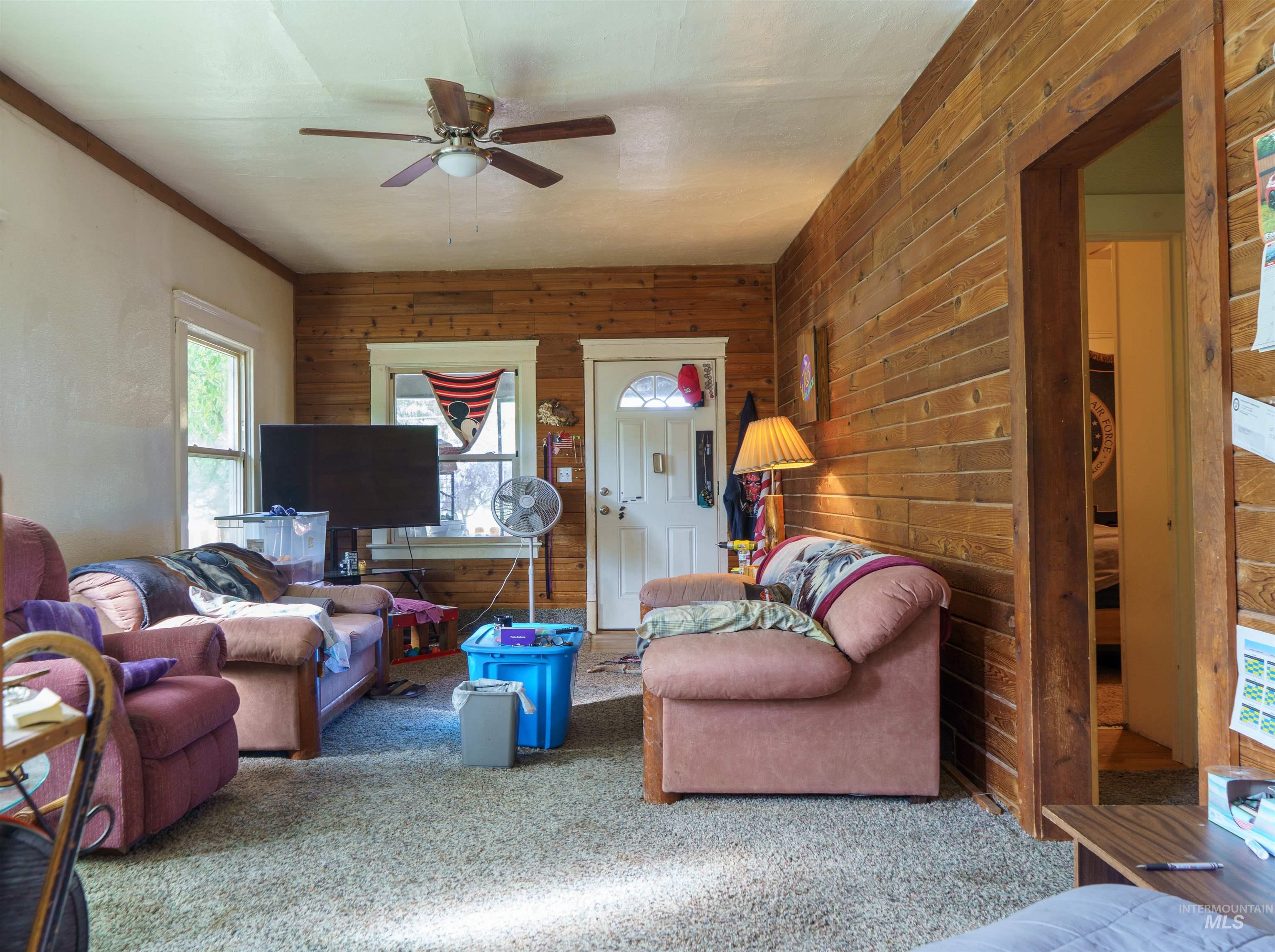 Carpeted living room with wood walls, ceiling fan, and ornamental molding