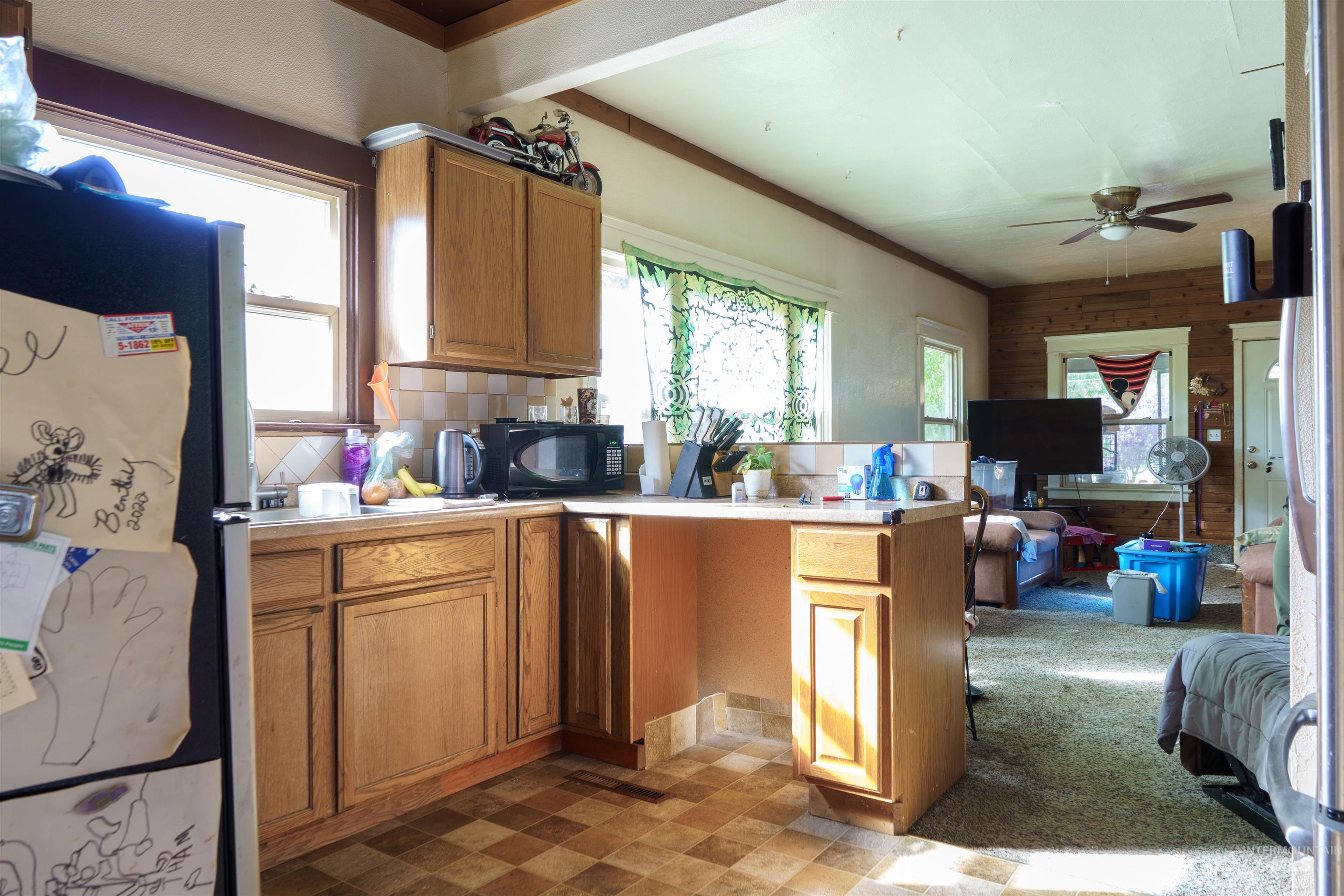 Kitchen with freestanding refrigerator, a peninsula, healthy amount of natural light, brown cabinetry, and wood walls